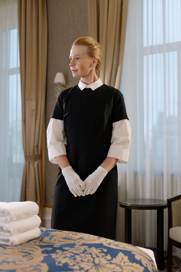 Chambermaid in uniform standing in hotel room with folded linens, exuding professionalism.